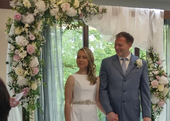 Couple getting married under a pink and white floral arch with draped voile.