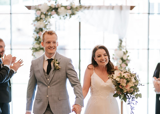 Just married couple with a pink and white bridal bouquet standing in front of a pink and white wedding arch.