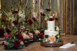 a burgundy and peach meadowscape of flowers frame a wedding cake at Cliveden House