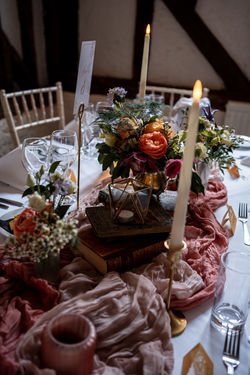 Candlesticks and stacked books surround bud vases and copper bowls filled with deep pink, orange and