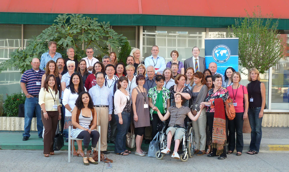 A group photograph of approximately 30 people taken outside a building, with two small trees in the background
