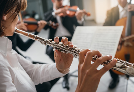 Professional female flustist playing her instrument on stage with classical music symphony