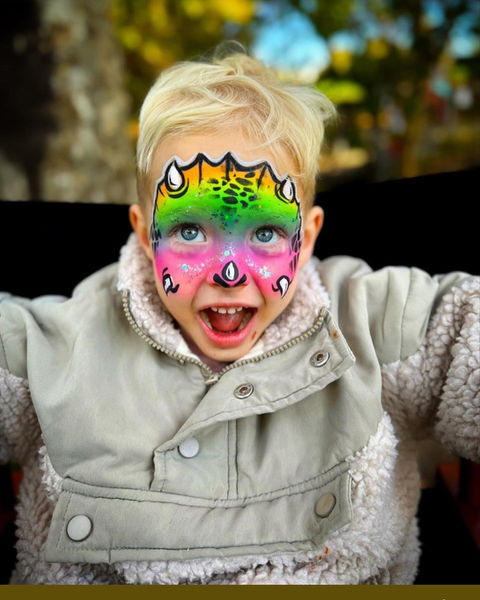 Boy with rainbow dinosaur face painting design at kid's birthday party in San Francisco