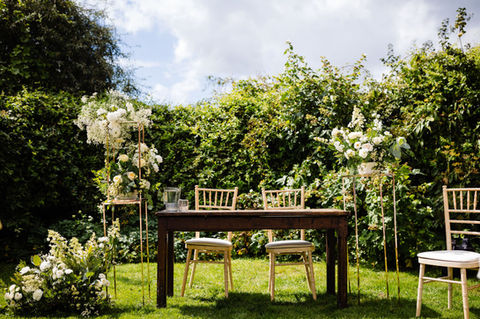 a signing table outside in a garden with floral arrangements either side of the table