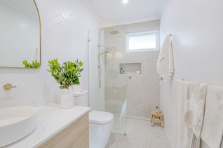 Beautifully renovated bathroom with gold fixtures, a glass shower, and light wood vanity, exuding a fresh and airy aesthetic.
