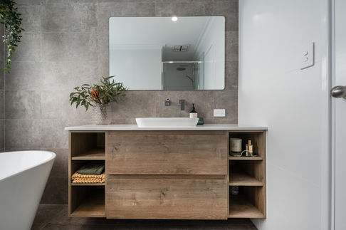 Modern bathroom vanity with a timber finish, while benchtop, and a large frameless mirror.