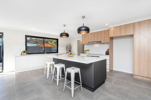 Contemporary kitchen renovation in Perth featuring a spacious island bench with a white stone countertop, dark customised cabinetry, light timber overhead cabinets, subway tile splashback, black and gold pendant lighting, and modern bar stools designed by Elite Makeovers.