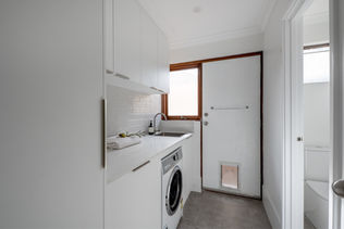 Laundry renovation with custom cabinetry, stone benchtop, and a built in front loader washing machine. The space includes a stainless steel sink, glossy subway tile splashback, and an external door with a pet flap for convenience.