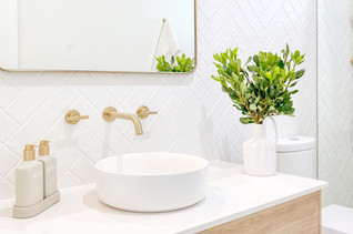 A spacious and elegant bathroom featuring white terrazzo tiles, gold tapware, and a glass shower screen. Designed by Elite Makeovers.