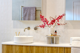 Close-up of a modern bathroom vanity with a round countertop basin, brushed brass wall-mounted tapware, and a floating timber cabinet. The space is styled with Australian native flowers and natural décor, enhancing the warm and elegant design. Renovated by Elite Makeovers, Perth’s leading bathroom renovation specialists.