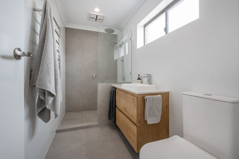 Modern bathroom renovation in Perth with a walk-in shower, rainfall showerhead, and timber vanity.