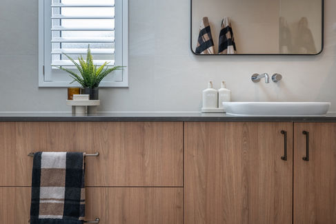 Modern bathroom vanity with a stone benchtop, stylish basin sink, and a decorative plant adding a touch of greenery. Soft neutral tones and natural light enhance the space.