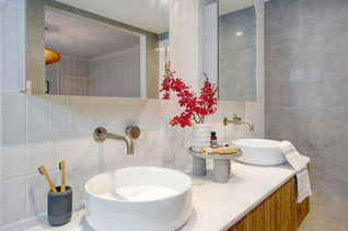 Side view of a modern bathroom vanity featuring twin round basins, brushed brass wall mounted tapware, and a floating timber cabinet. Styled with Australian native flowers and natural décor, this design combines warmth and sophistication. Renovated by Elite Makeovers, Perth’s trusted bathroom renovation specialists.
