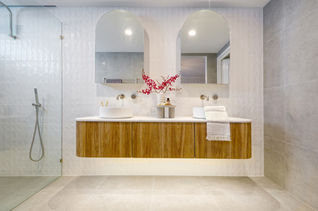 Front view of a Modern bathroom transformation in Perth Wembley Downs with a floating timber vanity, twin arched mirrors, and a walk-in shower. The textured wall tiles, and premium fittings add sophistication and warmth. Renovated by Elite Makeovers, specialists in high-end bathroom designs across Perth.