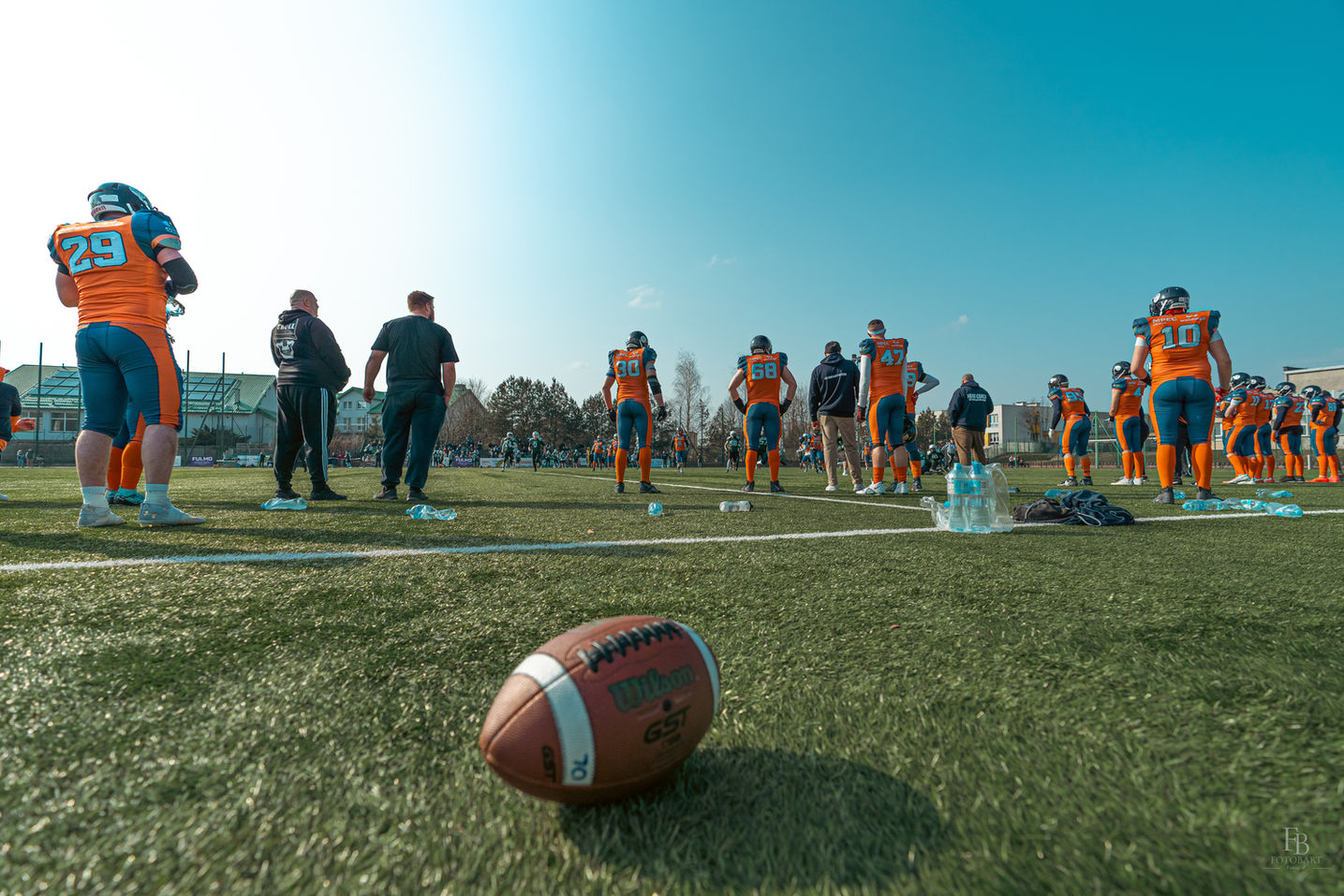 Laguppställning vid sidlinje med boll i förgrunden under match i amerikansk fotboll i Mellansverige.