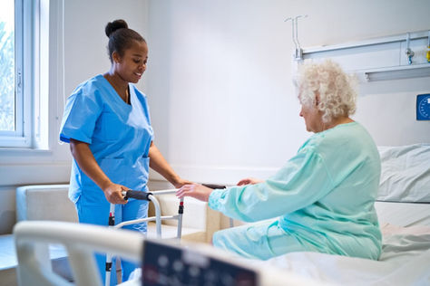 A nurse helps her patient in a skilled nursing facility use her walker.