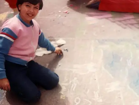Fotografia di me stessa da bambina, mentre disegno con un gessetto sull'asfalto, simbolo del gioco e dell'inizio dell'espressione artistica personale
