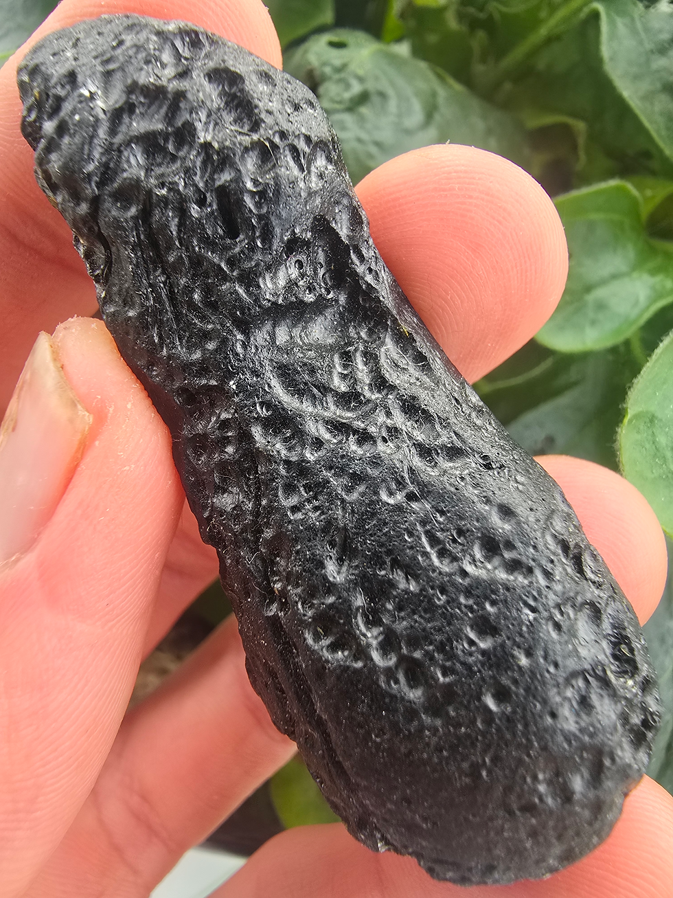 Thumbnail: Hand holding a rough, dark Vietnam Indochinite Tektite