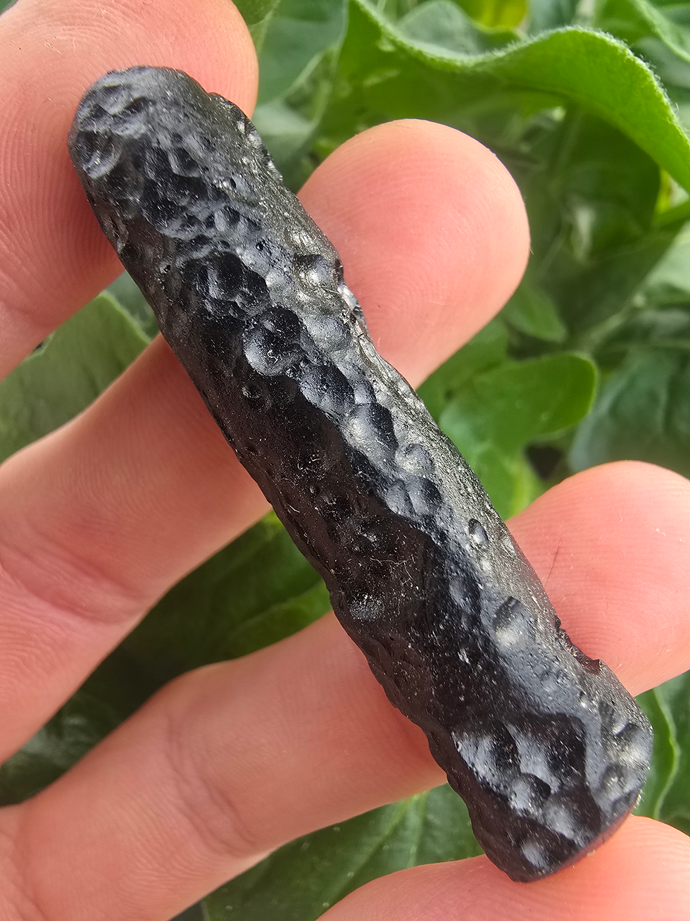 Thumbnail: Hand holding a dark, textured Indochinite tektite