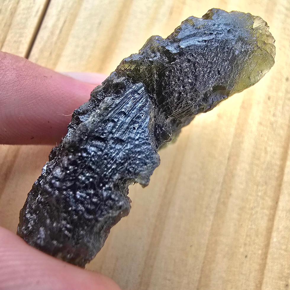 Thumbnail: Hand holding a rough, dark green moldavite stone
