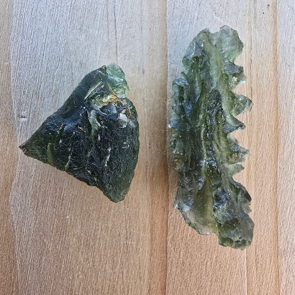 Dark green spiky and smooth Moldavite pieces shown on a wooden surface.