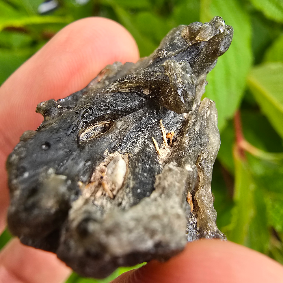 Thumbnail: Dark moldavite stone, 1.65g, held in hand.