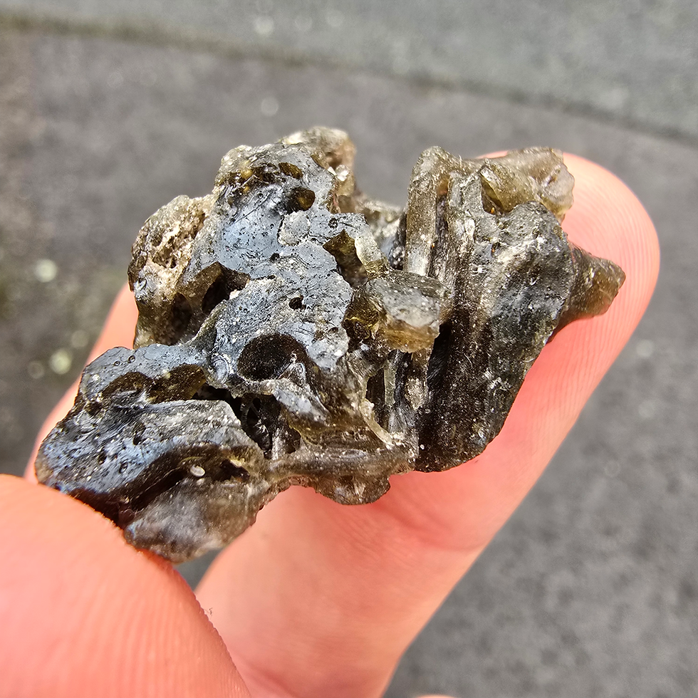 Thumbnail: Hand holding dark, textured 0.56g Moldavite