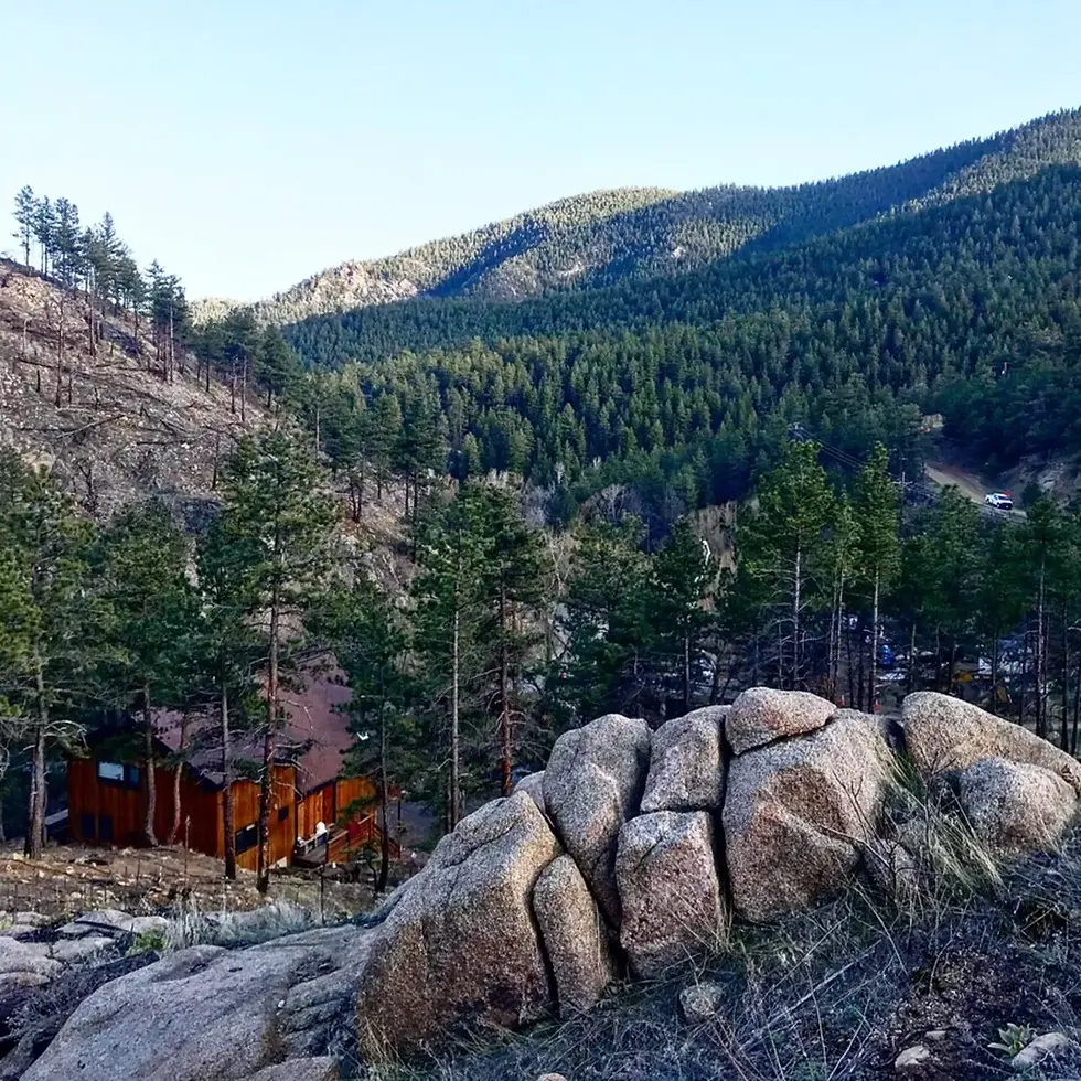 Mountain cabin with orange exterior surrounded by pine forests and granite boulders with valley views