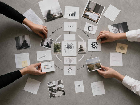 Top-down photo of hands arranging documents, data cards and photos into a circular pattern on a grey background, representing workplace burnout analysis and recovery supplement planning.