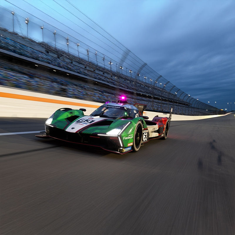 Race car with number 63 speeds along a track at dusk, featuring green, black, and white colors. Bright lights and a cloudy sky set the mood.