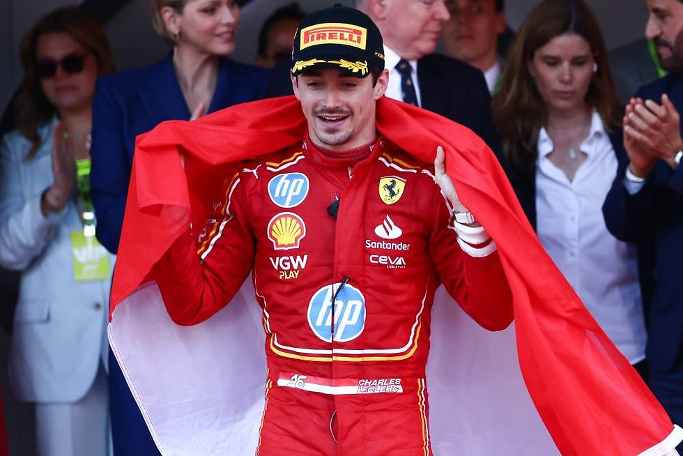 Race car driver celebrating with a red flag, wearing a red Ferrari suit and Pirelli cap. Smiling, surrounded by applauding people.