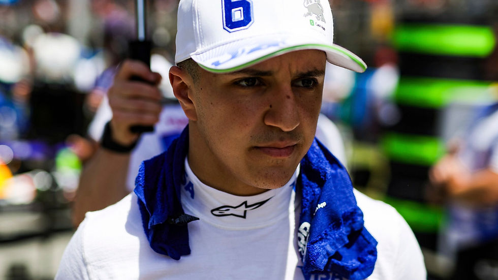 Man in a white cap with "6," blue towel around his neck, focused expression. Blurred background with bright colors. Racing ambiance.