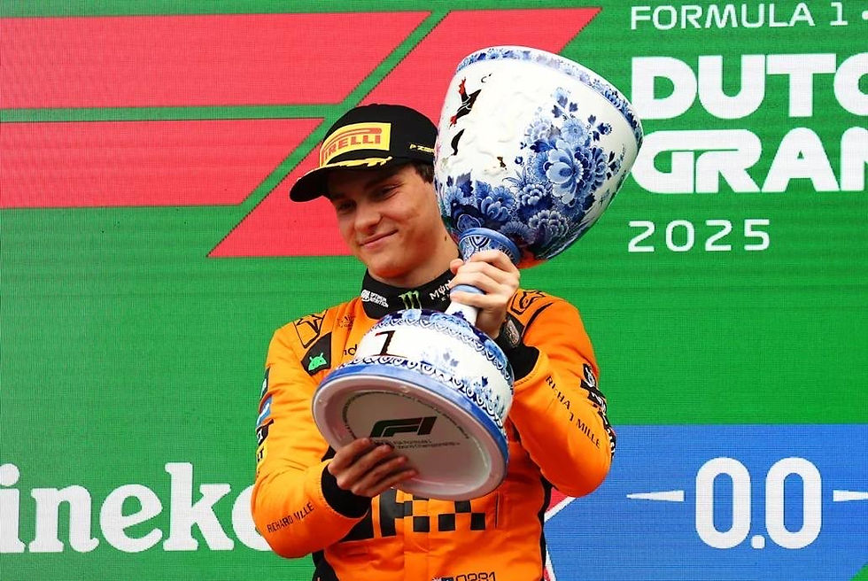 Race car driver in orange suit holds a large blue and white trophy, smiling on podium. Background shows "Formula 1 Dutch Grand Prix 2025".
