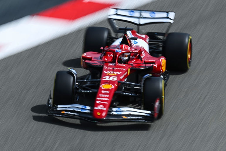 Red Formula 1 car with number 16 races on track. Driver in helmet focused. Sponsors' logos visible. Motion blur adds speed effect.