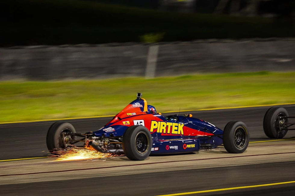 Race car with "PIRTEK" logo speeds on track, sparks flying from undercarriage. Night setting, blurred background, dynamic action.
