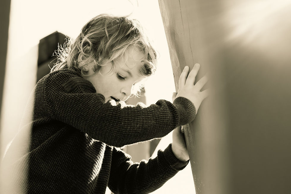 Young autistic child leaning against wall in sunlight, appearing overwhelmed and seeking sensory regulation during emotional moment.