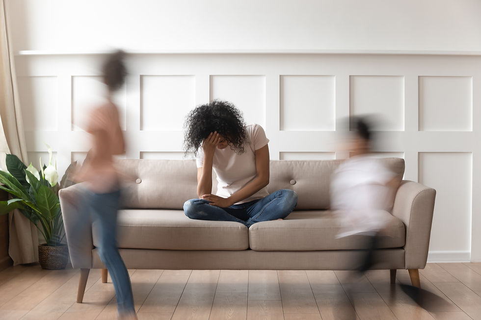 Overwhelmed mother sitting on couch with head in hand while children move quickly around her, illustrating caregiver stress and emotional overload in families navigating autism or behavioral challenges.