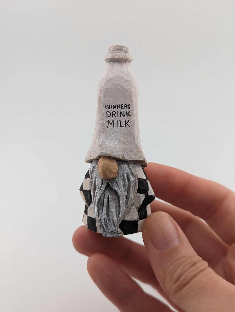 Thumbnail: wood carving of a gnome with a milk bottle shaped hat that says "winners drink milk"