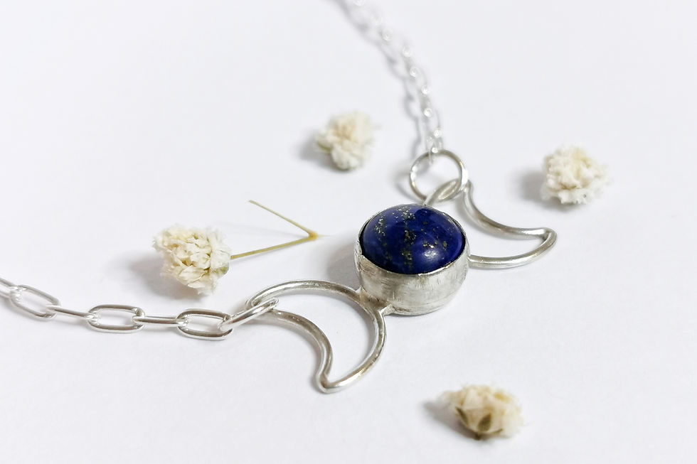 The Lapis Lazuli gemstone and sterling silver moon necklace with four dainty white dried flowers around the item.