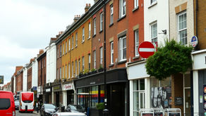 A sunlit residential street in South London with apartments and local businesses