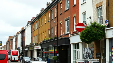 A sunlit residential street in South London with apartments and local businesses