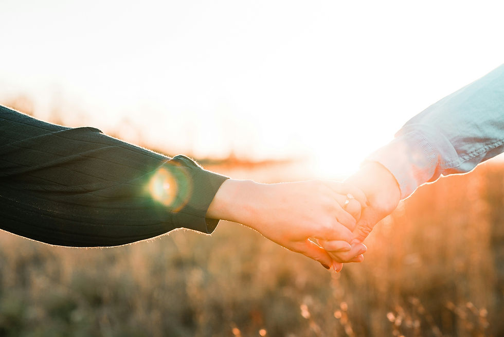 Two people holding hands, silhouetted against a bright sunset or sunrise in a field.