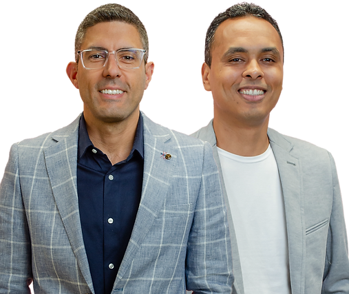 wo men standing side by side. On the left, Maykon, a white man with short gray hair, wearing transparent glasses, a light gray checkered suit, and a dark blue formal shirt. On the right, Wesley, a brown-skinned man with short gray hair, wearing a light gray blazer and a plain white t-shirt.