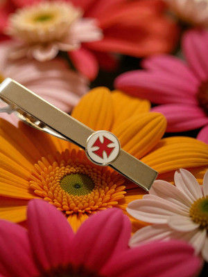 Pince-à-cravate templière – Croix templière émaillée rouge sur fond blanc sur fleurs colorées.