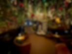 A wide view of The Waiting Room’s lounge showcasing string lights, hanging holiday decorations, and Christmas trees in the corners.