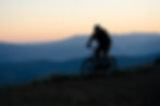 A photo of a person riding a bike. The background shows some blue mountains, and it looks like it is around sunrise or sunset.