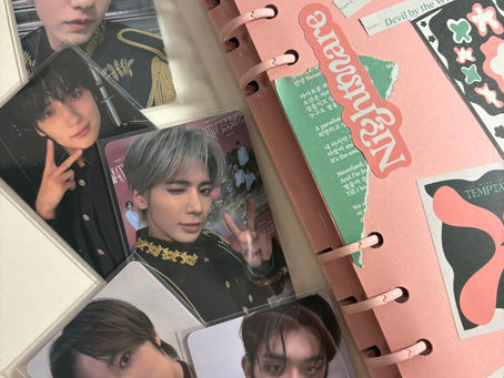 A flat-lay photograph of TXT fan collection items, including an open "The Name Chapter: TEMPTATION" album and assorted member photocards arranged around it.