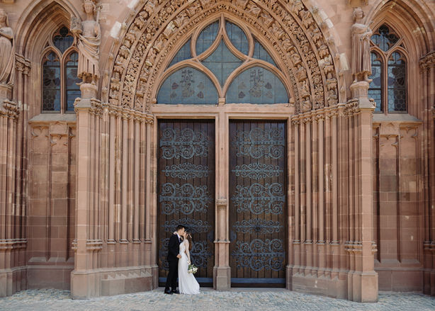 Zivilhochzeit in Basel. Brautpaar steht vor dem grossen Tür des Münster Basel, Gesamtaufnahme wo man das ganze Tor sieht