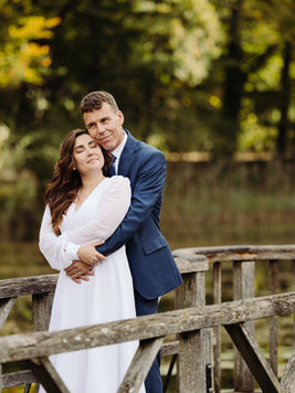 Brautpaar steht auf dem Steg beim See in der Eremitage Arlesheim, Bräutigam umarmt seine Braut