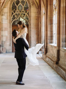 Bräutigam hebt seine Braut hoch und sie lacht. Fotoshooting im Kreuzgang Münster Basel,